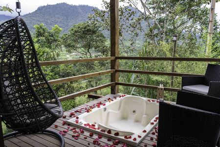 Outdoor bathtub bathtub on hotel balcony with mountain view. Pink petals are seen surrounding and some armchairs in the placeの写真素材