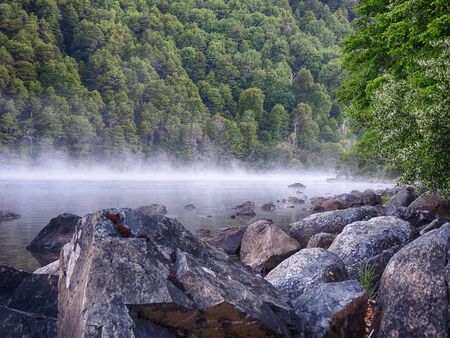 steam or mist over a lake. Large stones and a forest full of trees and pine trees are seen. Beautiful lake, Patagonia Argentinaの写真素材