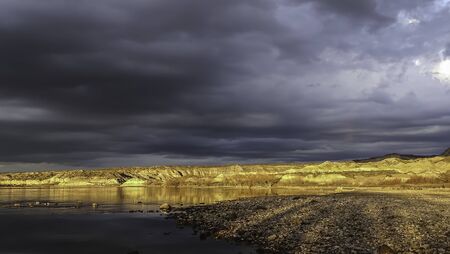 Valley of the yellow moon bordering a large river, surface of stones and a sky full of clouds. golden hour. Patagonia, Argentinaの写真素材