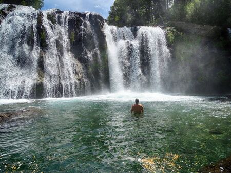 A man taking a bath in waterfalls. Crystal clear waters, there is a forest around.の写真素材