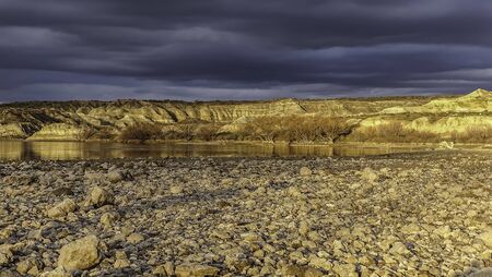 Yellow Valley of the Moon that borders a great river, a surface of stones and a sky full of clouds. golden hour Patagonia, Argentinaの写真素材