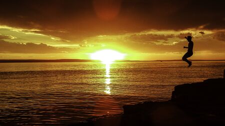 Man jumping into a lake at golden sunset. Summer holidaysの写真素材
