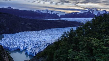 Panoramic view of the Gray Glacier, located inside Torres del Paine National Park. There are some trees on the right and large snowy mountains in the background. Sunset sky in autumn.の写真素材