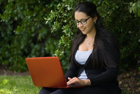 A woman is sitting on the grass studying with her laptop in the park. Natural environment. Educational conceptの写真素材