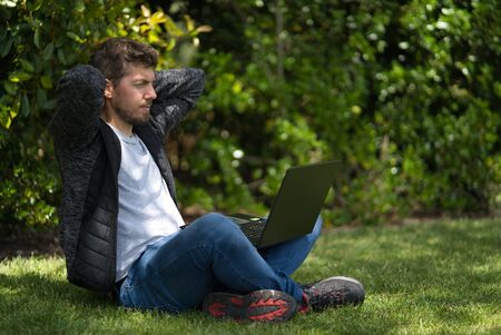 Young man looking at the screen of his computer with his hands behind his head like he is relaxing. Technological concept. Natural Environmentの写真素材