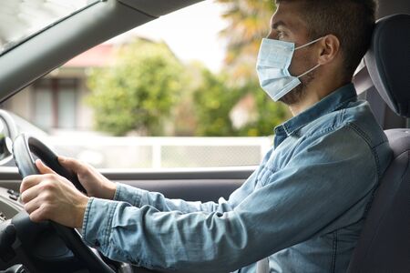 Young caucasian man wearing face mask driving her car. Covid-19 (Corona virus) conceptの写真素材