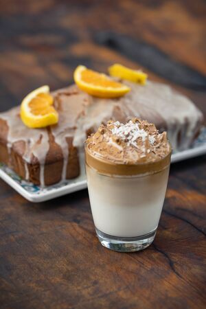 Whipped or Dalgona coffee served on a glass with a bar of chocolate and a wholemeal cake behind. Outdoor backgroundの写真素材