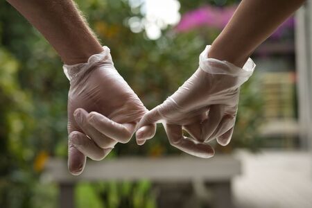 Hands holding each other with the little finger wearing sanitary gloves. Close up. COVID-19 conceptの写真素材