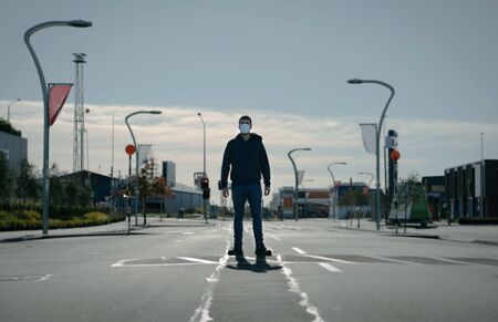 Young man wearing face mask standing in the middle of the road on an empty city centre. Coronavirus conceptの写真素材