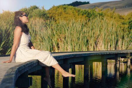 Woman sitting on a wooden walkway enjoying sunlight and admiring the landscape. Inspirational conceptの写真素材