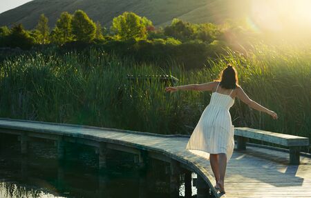 Woman balancing on a wooden walkway surrounded by water. Inspirational conceptの写真素材