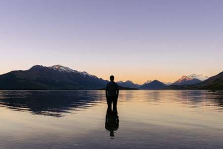 Man inside Lake Wakatipu looking at the amazing sunset behind snowy mountain peaks. New Zealand landscapeの写真素材