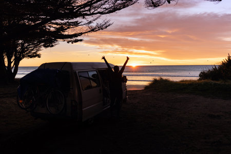 Young man waking up at sunrise by the beach next to his camper van. Van life concept.の写真素材
