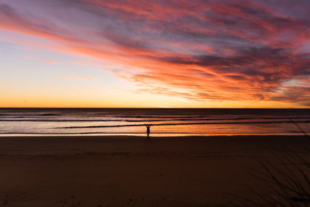 Woman silhouette at the beach during sunrise with dramatic pink sky. Inspirational conceptの写真素材