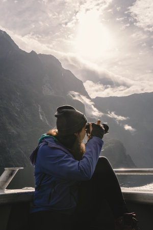 Woman taking photos with camera on a cruise on Milford Sound. Fiordland National Park, New Zealand.の写真素材