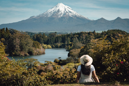Girl sitting on the grass looking at landscape with lake and Mount Taranki, New Zealand. Copy space photographyの写真素材