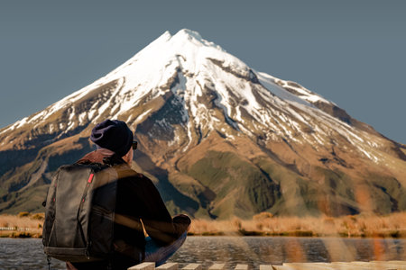 Young man sitting at the bottom of amazing snowy volcano. Copy spaceの写真素材