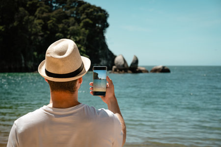 Tourist man taking a picture with mobile at Split Apple Rock. Abel Tasman National Park, New Zealand.の写真素材