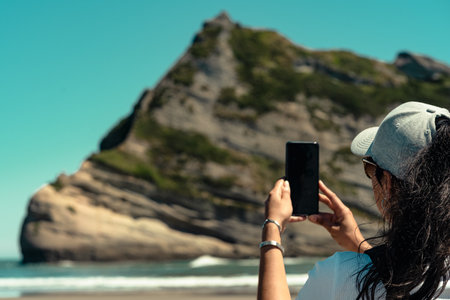 Woman taking picture with mobile in Wharariki beach, New Zealand.の写真素材