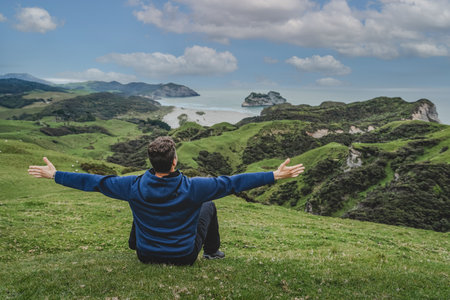 Young man with open arms at Wharariki beach lookout. New Zealand landscape.の写真素材