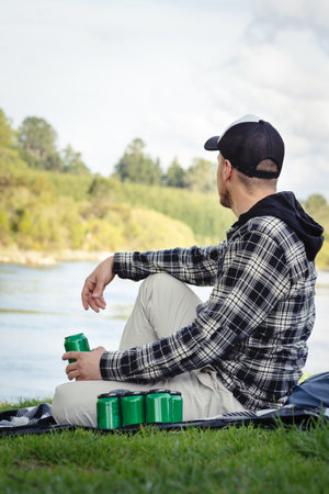 Man looking at the river and drinking beer on a park. Vertical photographyの写真素材