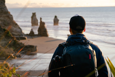 Young man with photographer backpack looking at scenic view of limestone formations by the beachの写真素材