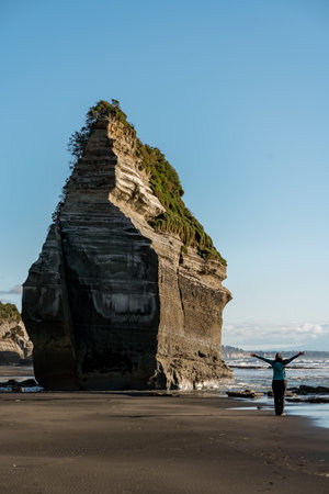 Woman on the beach next to a big rock formation known as one of the "Three Sisters". Located in New Plymouth, New Zealandの写真素材