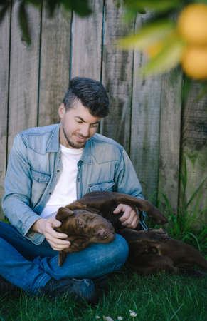 Man sitting on the grass playing with his dog on the garden. Portrait vertical photographyの写真素材