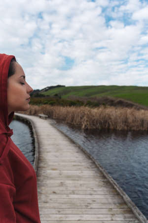 Woman wearing hoodie closes her eyes on a lake. Inspirational concept. Vertical photographyの写真素材