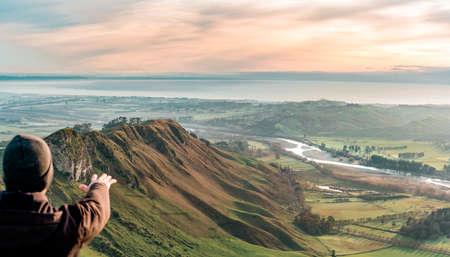 Young man at the top of a mountain extending his hand. Vertical photography, travel concept.の写真素材