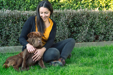 Young latin woman is sitting on the grass next to her dog. Domestic animals conceptの写真素材