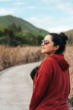 Hispanic woman on wooden walkway during autumn. Wetland environment. vertical portraitの写真素材
