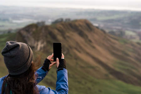 Brunette woman backwards taking a photo from the peak of a mountain during winter. Copy space. Travel conceptの写真素材