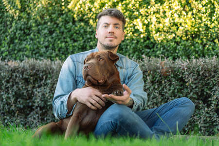Caucasian young man and his dogmposing sitting on the garden. Portrait photographyの写真素材
