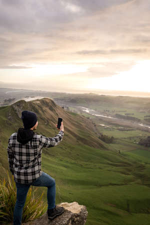 Young man taking a photo at the landscape. Vertical photography. Technology and travel conceptの写真素材