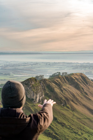 Young man at the top of a mountain extending his hand. Vertical photography, travel concept.の写真素材