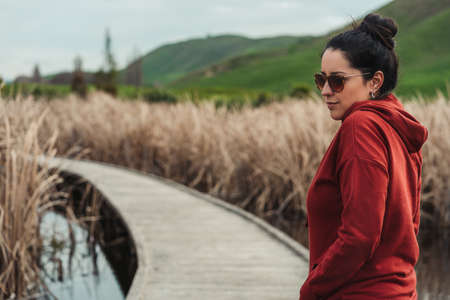 Hispanic woman on a wooden walkway. Portrait photography with copy space. Rural autumn landscape.の写真素材