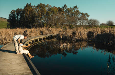 young couple sitting on boardwalk in lake shore and looking at mobile phone. Peka Peka Wetlands, Hawke's Bay, New Zealand.の写真素材