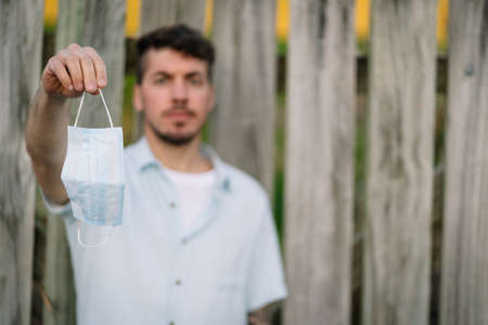Caucasian man hanging a medical face mask on his hand on an open air environment. Virus prevention conceptの写真素材