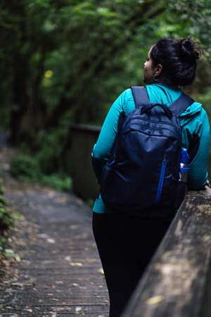 Woman standing on the side of a bridge in the middle of the woods. Ecotourism concept. Vertical photographyの写真素材