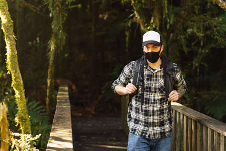 Man wearing face mask on a wooden bridge on the forest. New tourism during Covid-19 pandemic disease conceptの写真素材