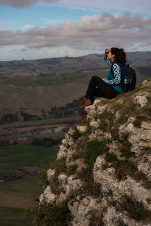 Brunette woman sitting at the top of a mountain and contemplating the landscape. Travel concept. Vertical photographyの写真素材