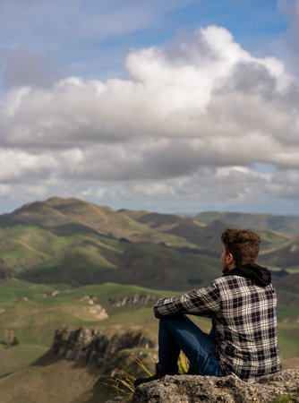 Caucasian man sitting at the top of the mountain and contemplating the landscape. Vertical photographyの写真素材