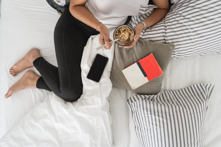 Top view of woman lying on bed while having breakfast on a pot with muesliの写真素材