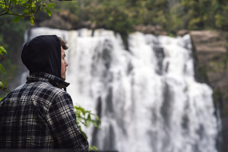 Young man wearing hoodie and admiring the nature in waterfall landscape. Inspirational conceptの写真素材