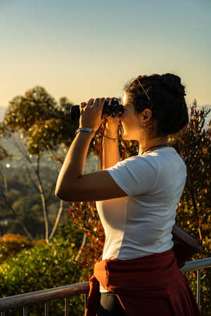 Brunette woman using binoculars on lookout during sunset. Vertical photographyの写真素材