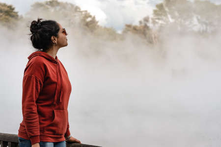 Young brunette woman admiring the beauty of a big hot pool in a place with geothermal activity. Copy spaceの写真素材