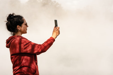 Woman taking photograph with mobile in place full of geothermal steam. Volcanic activity.の写真素材