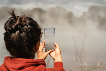 Woman taking photo with mobile phone at a place full of steam due to volcanic activity. Copy spaceの写真素材