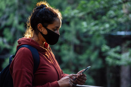 Young man holding mobile phone and wearing face mask on a natural environment. Covid-19 outbreak and communication concept.の写真素材